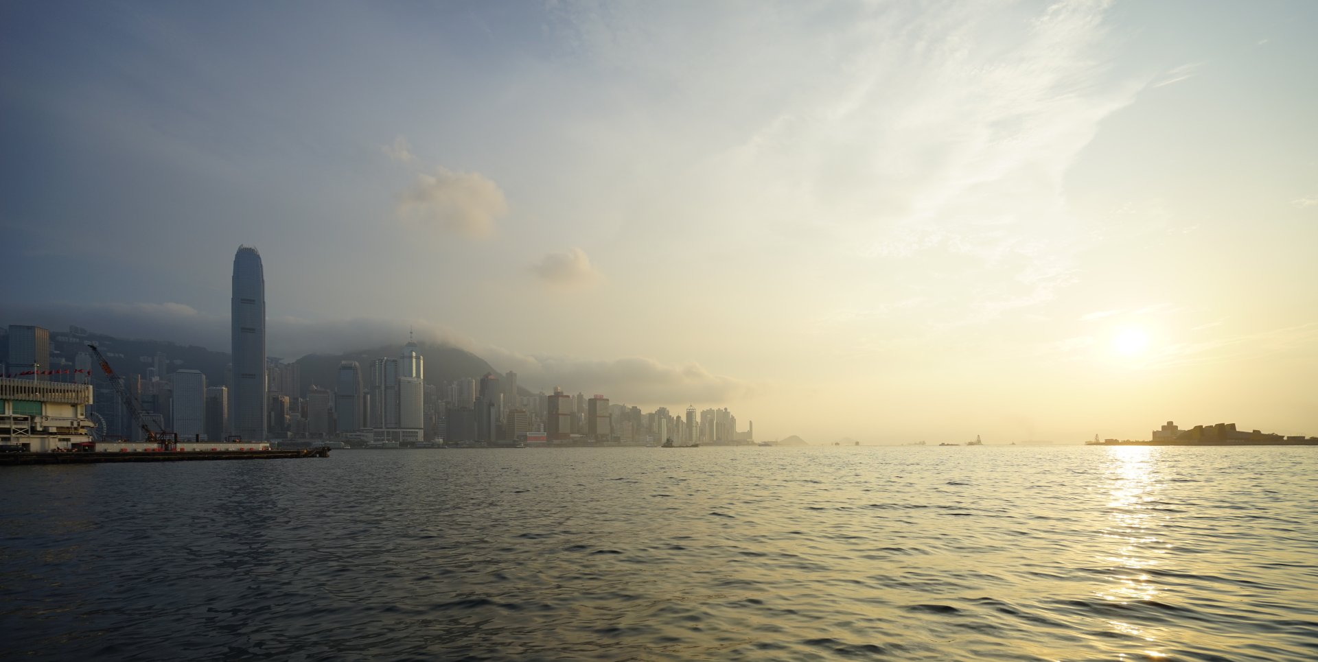 Victoria Harbour, Hong Kong: man-made skyline of high-rises along the sea beneath a hazy, sunlit sky — 5K Ultra HD PC desktop wallpaper.