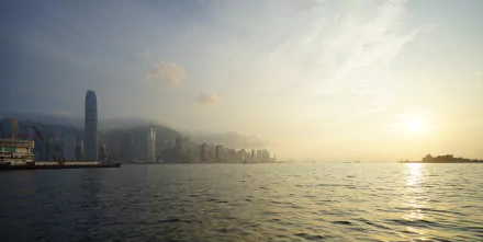 Victoria Harbour, Hong Kong: man-made skyline of high-rises along the sea beneath a hazy, sunlit sky — 5K Ultra HD PC desktop wallpaper.