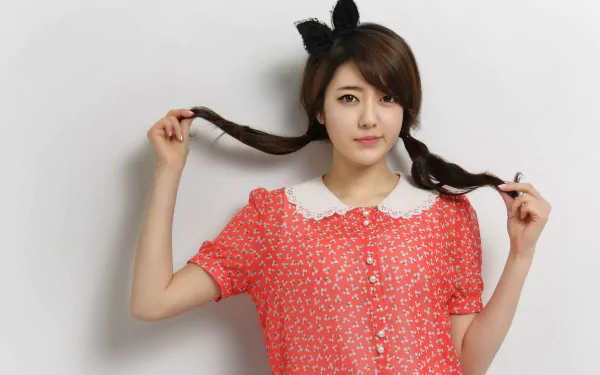 An Asian woman with a plait hairstyle poses confidently against a white background. She wears a red patterned dress with a white collar and black bow headband. HD desktop wallpaper and background.