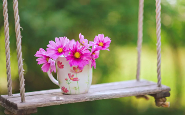 A 4K Ultra HD image of a bouquet of pink spring flowers in a floral cup resting on a wooden swing, set against a blurred green background.