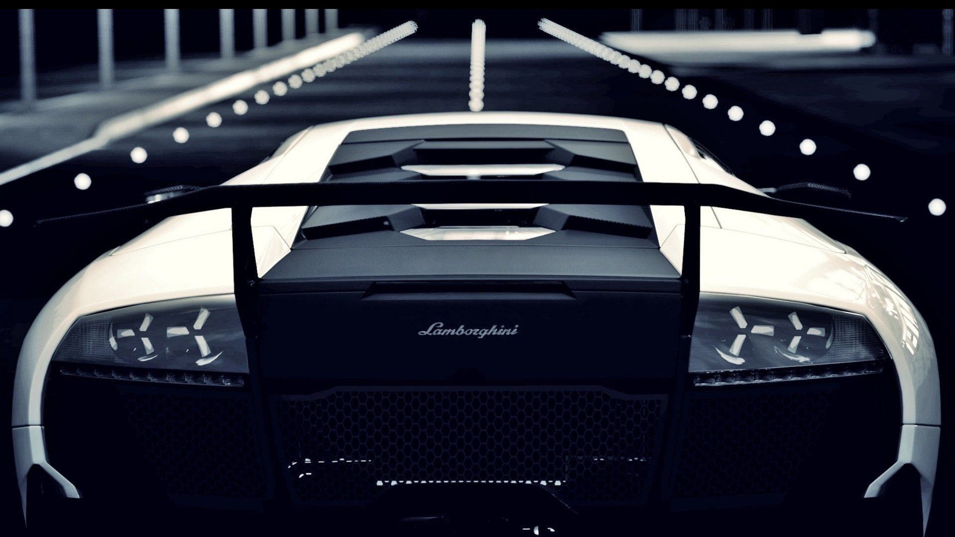 HD desktop wallpaper of a white Lamborghini Murciélago showcasing the rear view of this sleek, high-performance vehicle in a dimly lit setting.