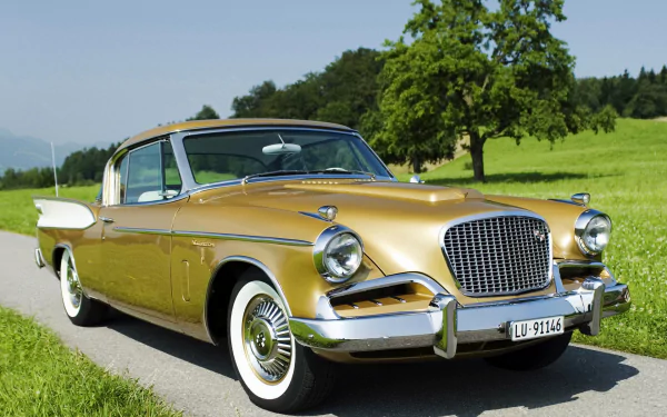 Gold Studebaker classic car parked on a country road with green fields and trees — HD PC desktop wallpaper/background of a vintage vehicle.