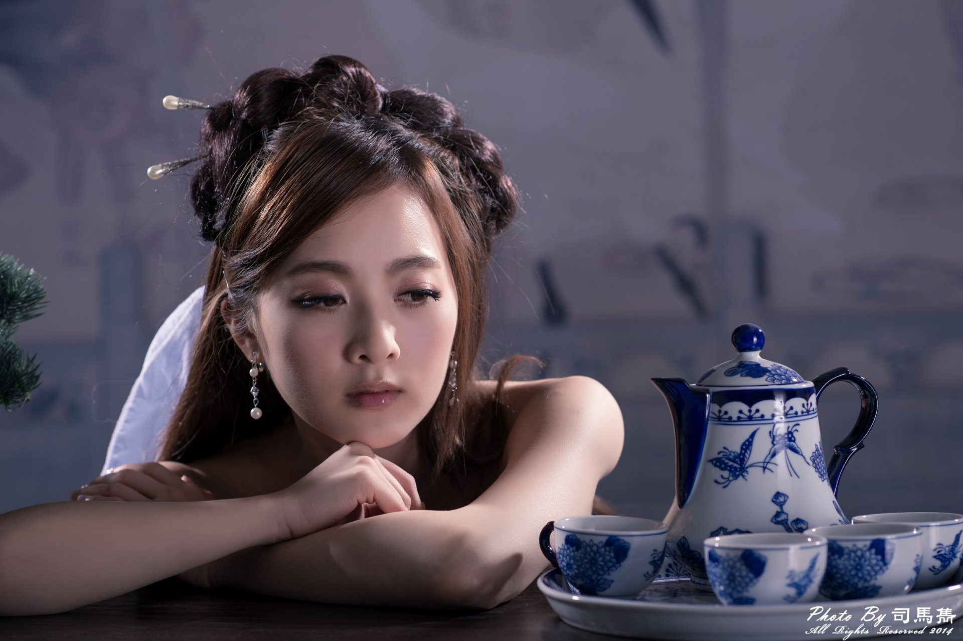 A Taiwanese woman with traditional Chinese hairpin and earrings sits pensively beside a blue and white tea set, captured in 4K Ultra HD quality.