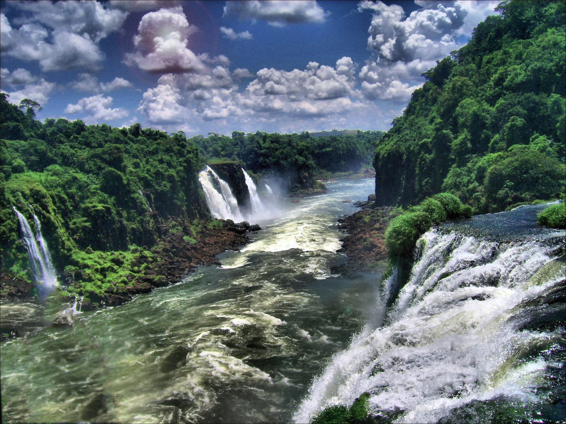 A breathtaking view of Iguazu Falls in Brazil, featuring cascading waterfalls surrounded by lush greenery and a vibrant sky filled with clouds, capturing the beauty of nature.