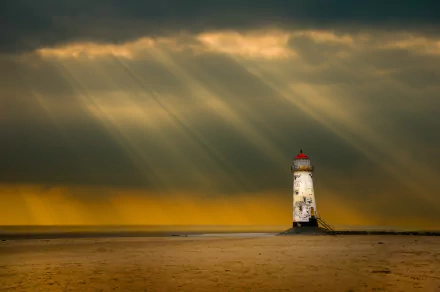 A striking lighthouse stands alone against a dramatic sky, with beams of light breaking through clouds. This 4K Ultra HD image serves as a captivating desktop wallpaper.