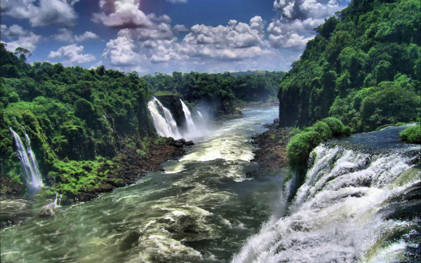 A breathtaking view of Iguazu Falls in Brazil, featuring cascading waterfalls surrounded by lush greenery and a vibrant sky filled with clouds, capturing the beauty of nature.