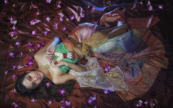 A Thai woman in traditional costume poses gracefully among vibrant flowers, showcasing intricate jewelry, with a rich, colorful backdrop, creating a captivating oriental ambiance.