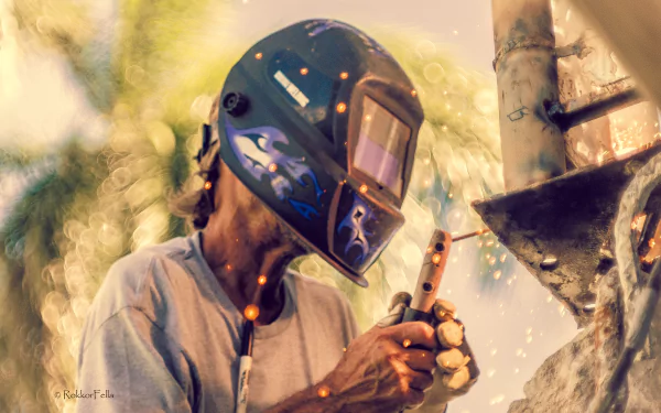 A welder wearing a protective helmet sparks bright welding in a bokeh-lit scene, captured in stunning 4K Ultra HD quality as a PC desktop wallpaper.