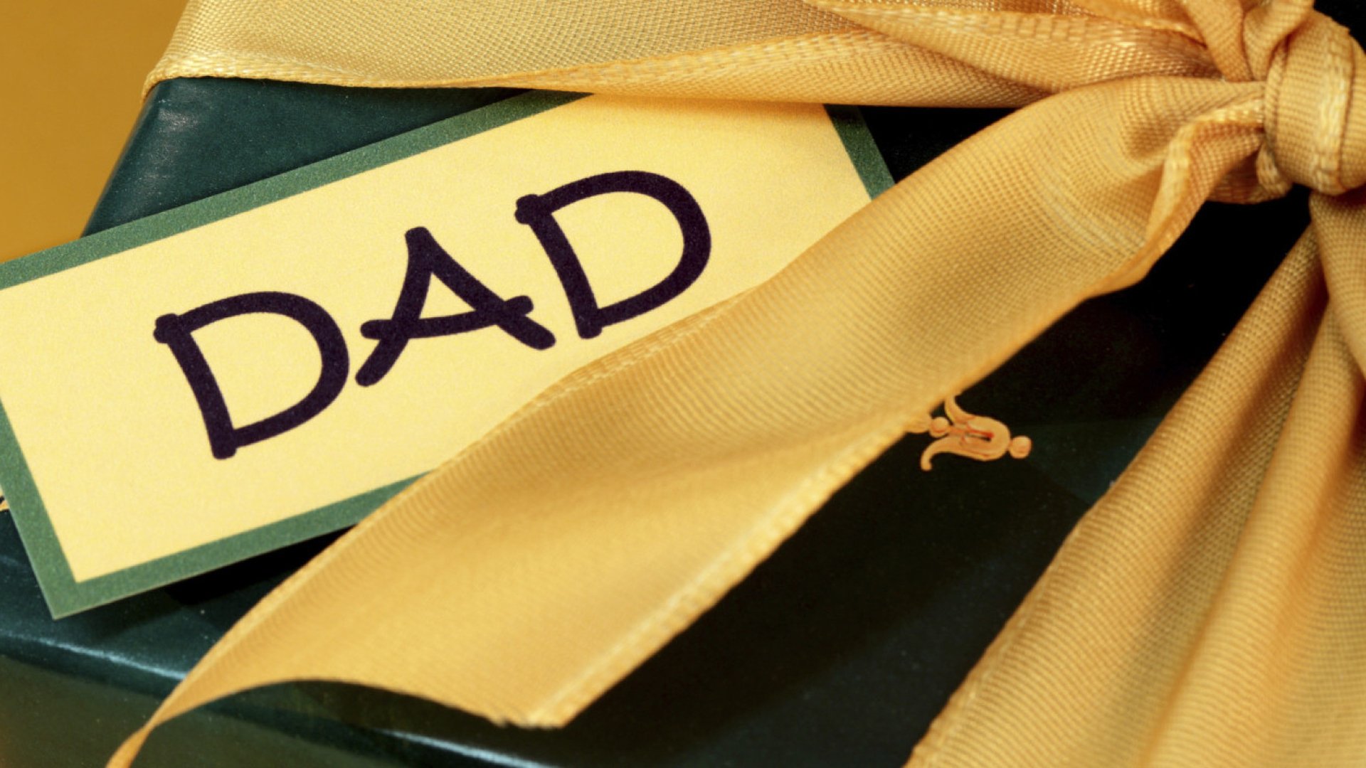 A close-up of a gift wrapped in green with a yellow ribbon, featuring a tag that reads DAD, celebrating Father's Day. This image makes a charming HD desktop wallpaper.