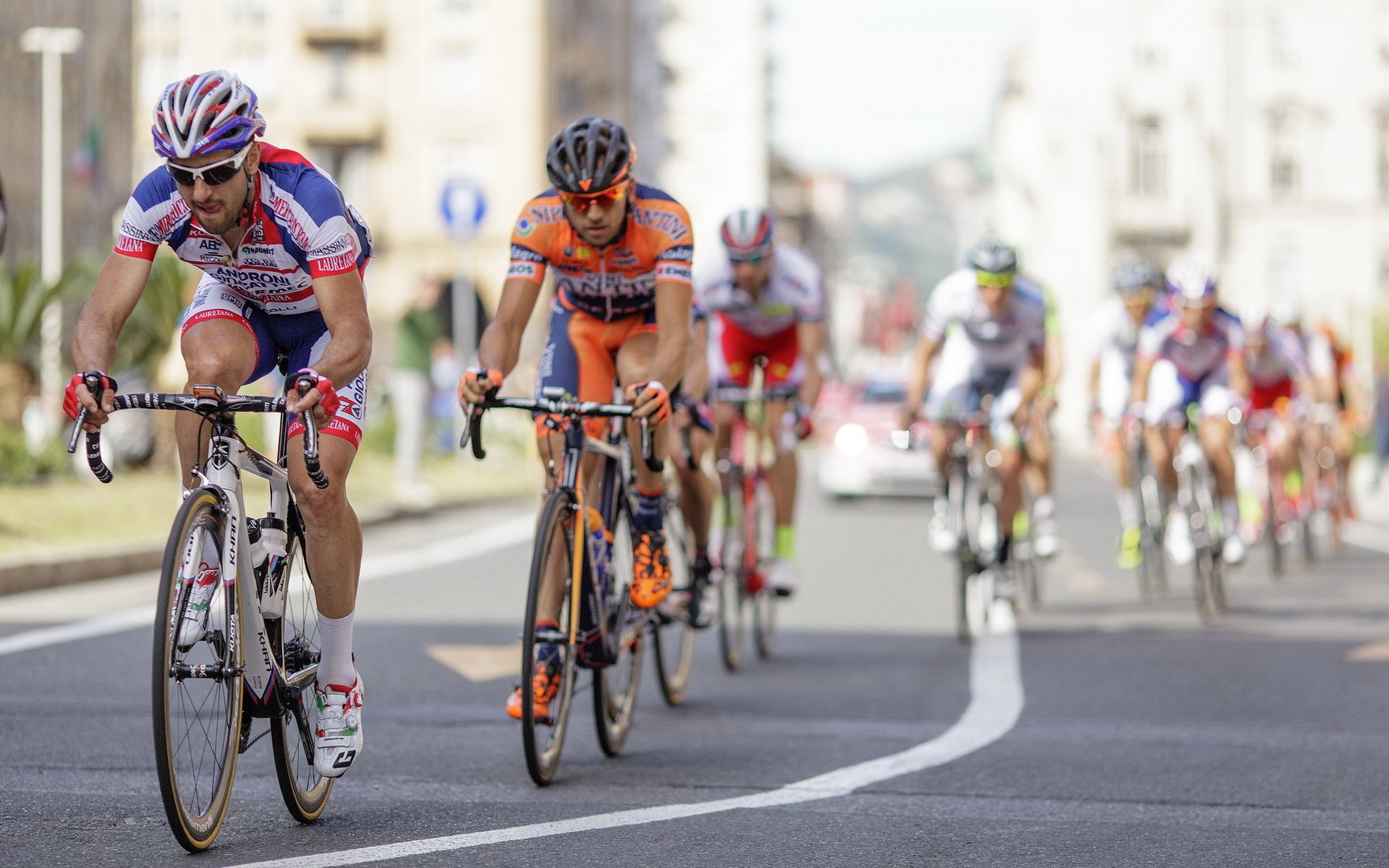 HD desktop wallpaper capturing a dynamic cycling race with athletes competing intensely on a city street, showcasing the spirit of sports and endurance.