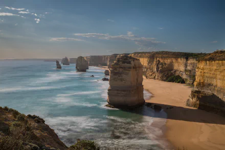 4K Ultra HD view of The Twelve Apostles limestone stacks casting shadows on the sandy coastline along the sea in Victoria, Australia.