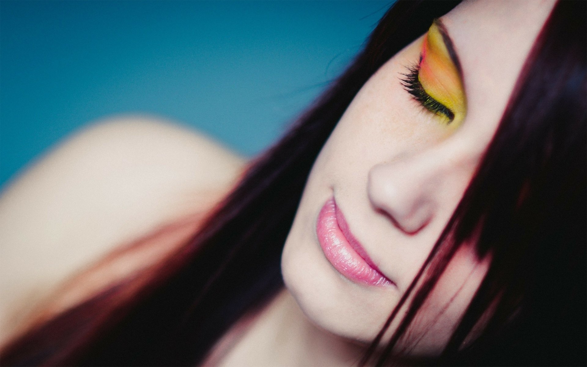 Close-up of a woman with vibrant yellow eyeshadow and long dark hair, showcasing artistic makeup. The image serves as an HD desktop wallpaper and background.