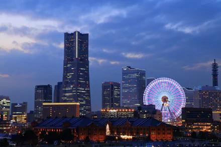 Night view of Yokohama city skyline in Japan featuring illuminated skyscrapers and a brightly lit ferris wheel against a deep blue evening sky.