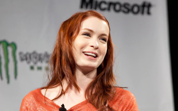 Smiling red‑haired actress onstage in an orange top, captured as a 4K Ultra HD PC desktop wallpaper.