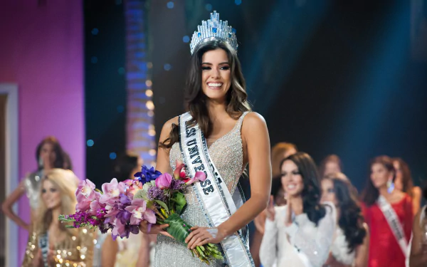 Paulina Vega, Miss Universe, proudly holds a bouquet of flowers while wearing her crown during the pageant, surrounded by fellow contestants, showcasing elegance and celebration.