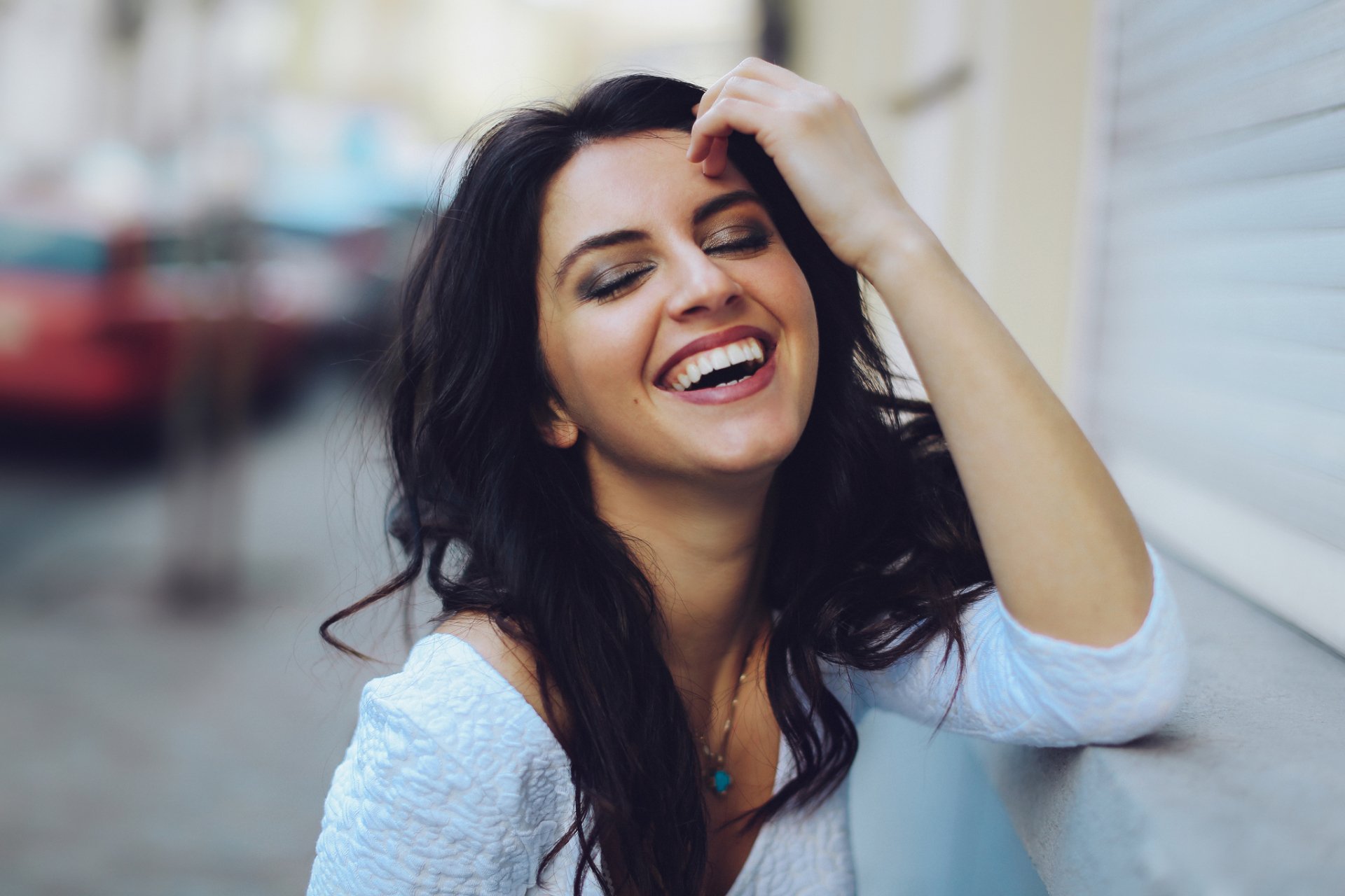 HD desktop wallpaper of a smiling brunette woman with a joyful mood, captured as a stylish model in an urban setting.