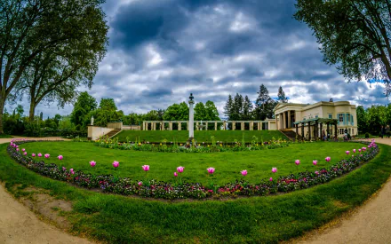 HD PC desktop wallpaper of Charlottenhof Palace: man-made neoclassical building with a formal rose garden, paths and trees beneath a dramatic cloudy sky.