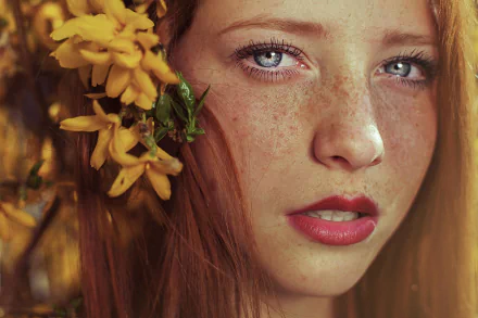 Close-up portrait of a redhead woman with blue eyes and freckles, adorned with yellow flowers, captured in HD for a striking desktop wallpaper background.