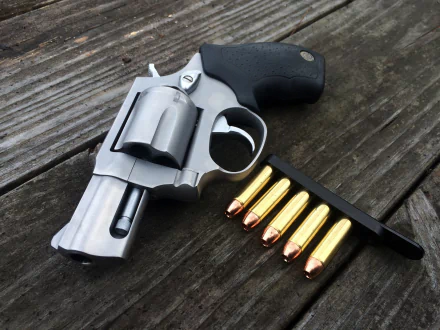 A close-up of a revolver resting on a wooden surface, accompanied by five golden bullets and a speed loader, designed as an HD PC desktop wallpaper and background.