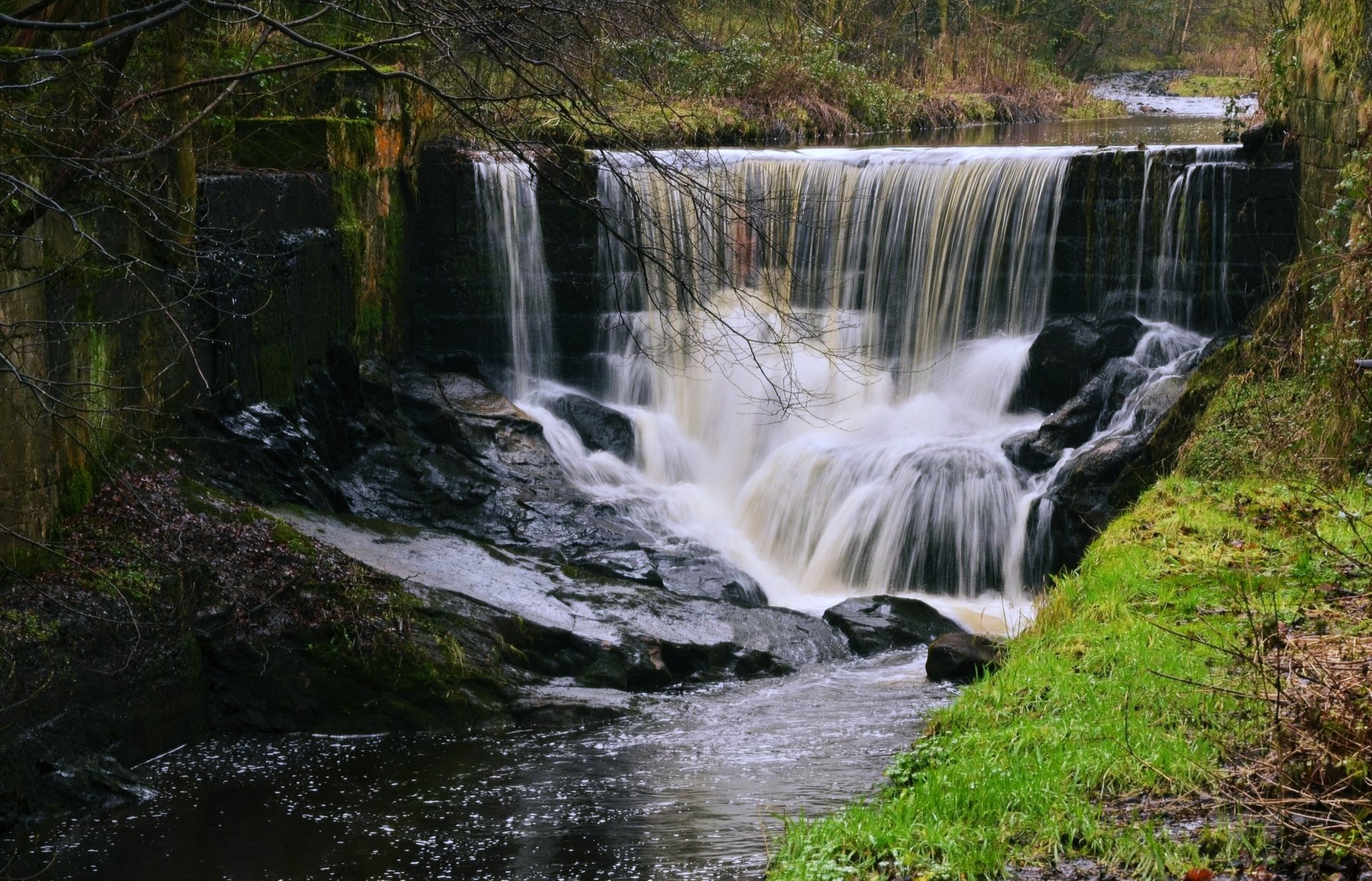 A serene landscape featuring a river cascading over a waterfall surrounded by greenery, captured in stunning 4K Ultra HD quality for a PC desktop wallpaper.
