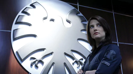 HD desktop wallpaper of a character from the TV show Agents of S.H.I.E.L.D., standing confidently in front of the iconic S.H.I.E.L.D. eagle emblem.