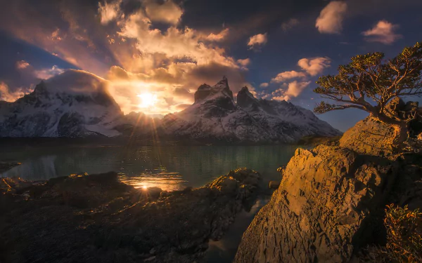 Sunbeam casts golden light over towering mountains and trees at Torres del Paine, Patagonia, reflecting on the tranquil lake in this HD nature desktop wallpaper.