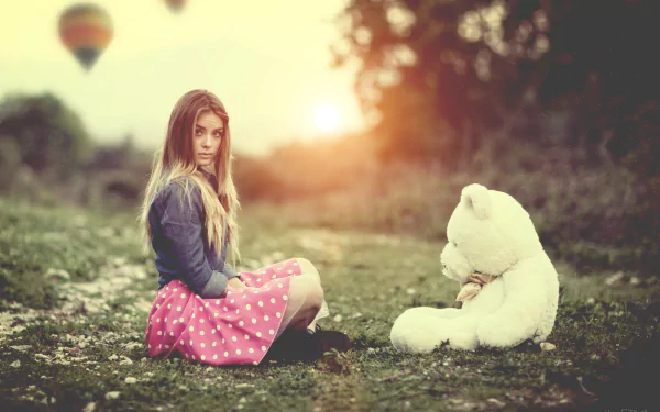 HD wallpaper featuring a blonde woman in a polka-dot skirt sitting opposite a teddy bear, with a blurred background including a hot air balloon.