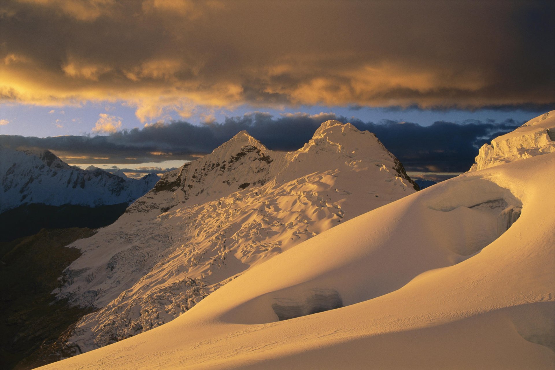 Stunning winter landscape featuring snow-capped mountains under dramatic clouds, providing a serene and picturesque nature scene for an HD desktop wallpaper.