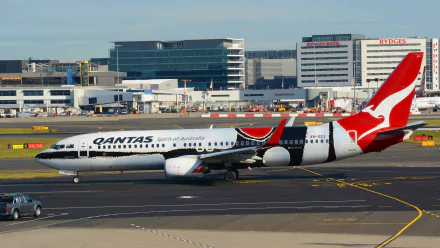 A Qantas Boeing 737 aircraft taxiing at Sydney Airport, showcasing Australia's iconic airline against a backdrop of modern terminal buildings.