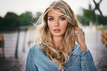 HD desktop wallpaper of a blonde woman with green eyes and a blue top, posing outdoors. The background is slightly blurred, emphasizing her features.