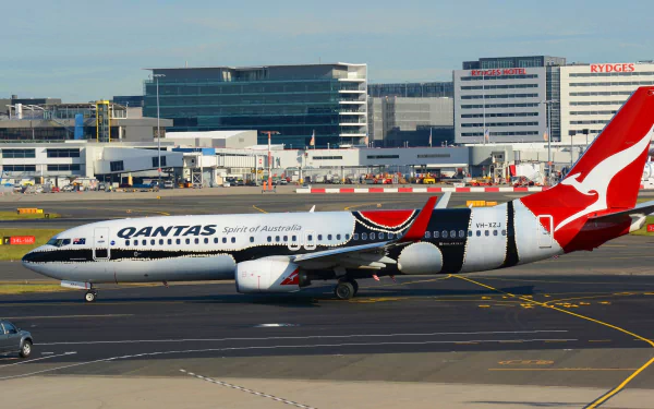 A Qantas Boeing 737 aircraft taxiing at Sydney Airport, showcasing Australia's iconic airline against a backdrop of modern terminal buildings.