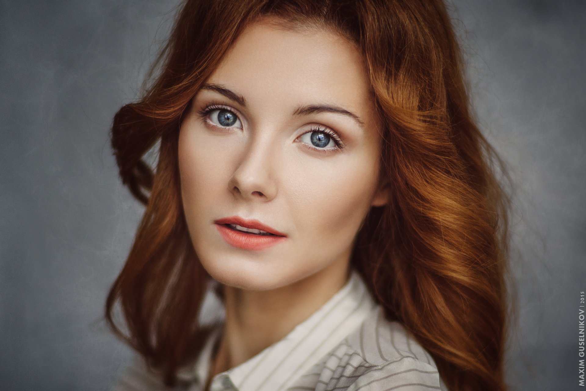A striking redhead woman with blue eyes poses softly, showcasing her natural beauty in this HD desktop wallpaper and background.