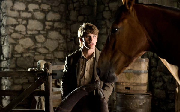 HD desktop wallpaper featuring a scene from the movie War Horse, showing a young man and a horse inside a rustic stone stable.