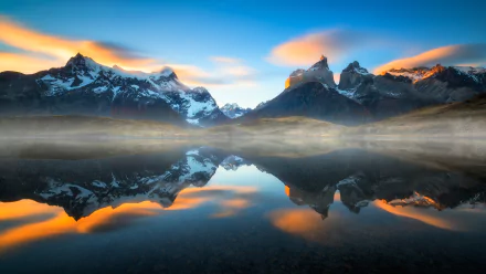 Sunset over foggy Torres del Paine mountains in Chile, reflected in a calm lake, showcasing a stunning natural landscape.