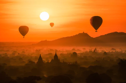 HD PC desktop wallpaper: sunset landscape photograph of the sun above fog-filled valleys, silhouetted temple spires and floating hot air balloons.