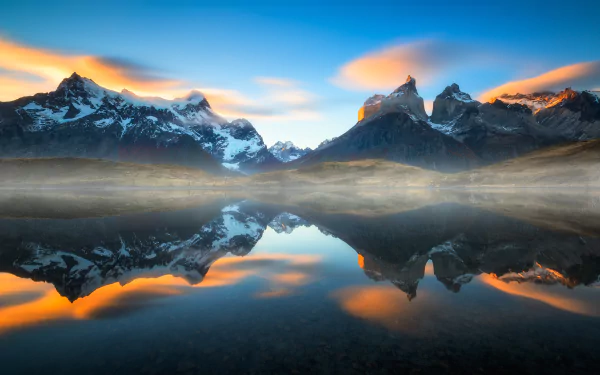 Sunset over foggy Torres del Paine mountains in Chile, reflected in a calm lake, showcasing a stunning natural landscape.