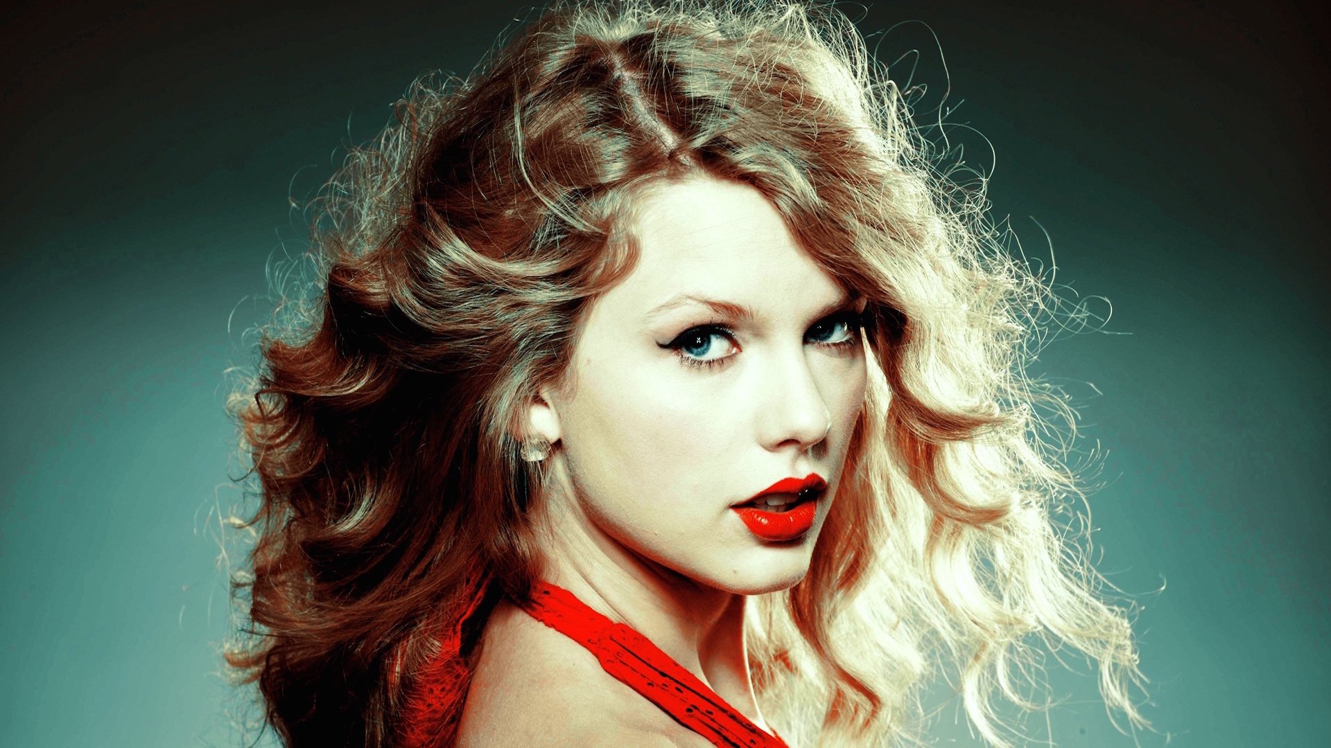 A vibrant HD desktop wallpaper featuring Taylor Swift with striking red lips and voluminous curls, capturing her dynamic presence in music.