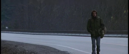 Quiet First Blood movie scene: lone man in a green jacket walks an empty roadside at dusk — 2K Quad HD PC desktop wallpaper/background.