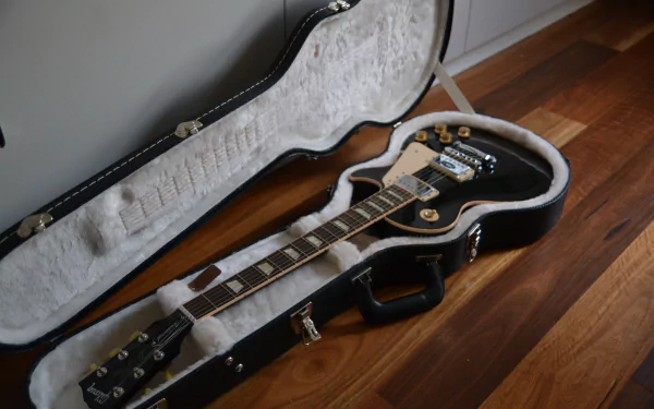 4K Ultra HD PC desktop wallpaper: electric guitar in open hardshell case on a hardwood floor, close-up of fretboard and pickups — music, guitar.