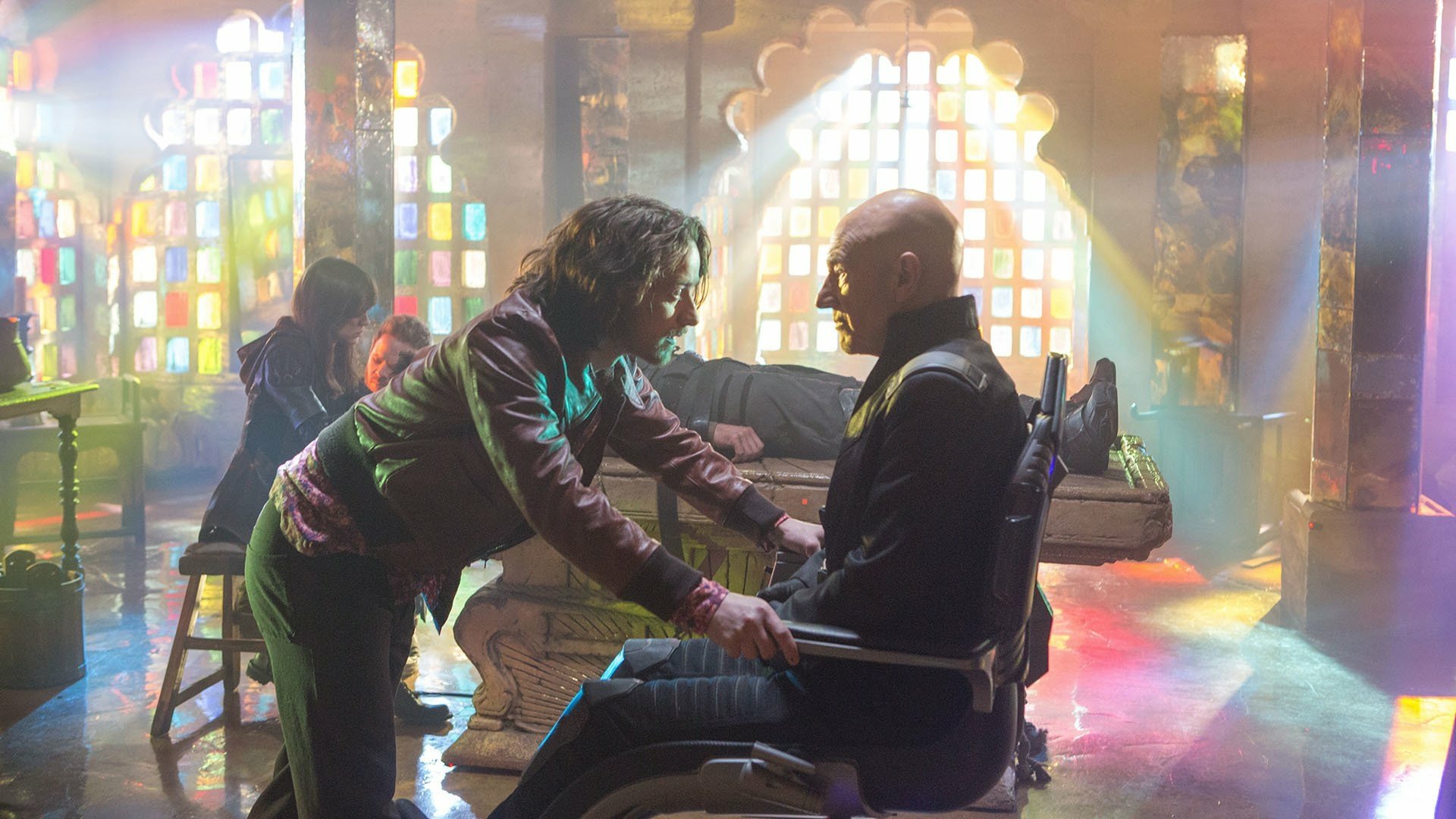 HD PC desktop wallpaper: movie still from X-Men: Days of Future Past — a woman leans toward a man in a wheelchair in a colorful, sunlit room.