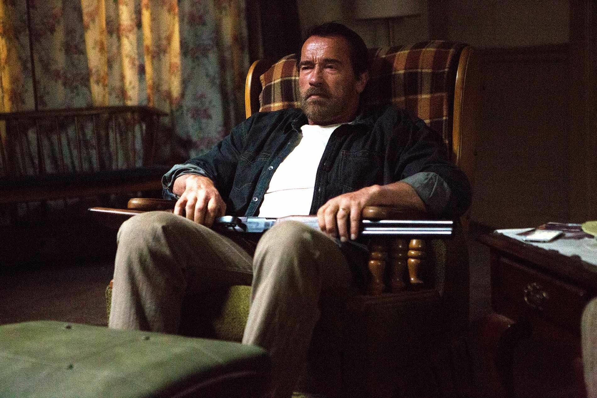 HD PC desktop wallpaper from the movie Maggie (2015): weary man in a plaid armchair holds a shotgun across his lap in a dim, cluttered living room.
