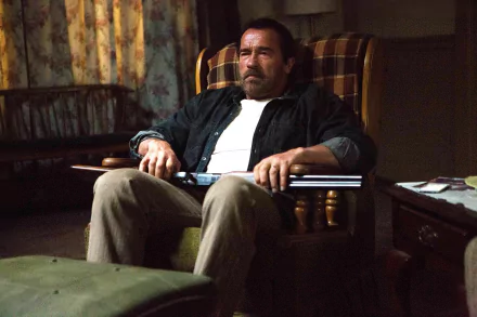 HD PC desktop wallpaper from the movie Maggie (2015): weary man in a plaid armchair holds a shotgun across his lap in a dim, cluttered living room.