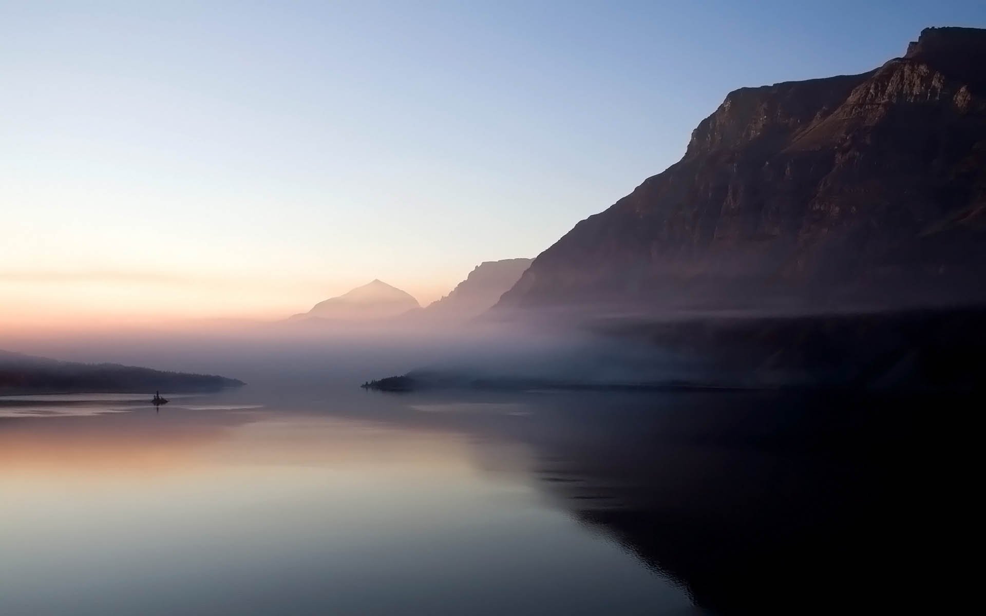A serene landscape featuring a river winding through cliffs, enveloped in fog, with majestic mountains in the background, creating an atmospheric nature scene for an HD wallpaper.