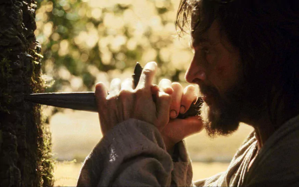 HD PC desktop wallpaper showing a bearded actor in a scene from the movie The Fountain, pressing a dagger into a mossy tree as sunlight filters through the leaves.