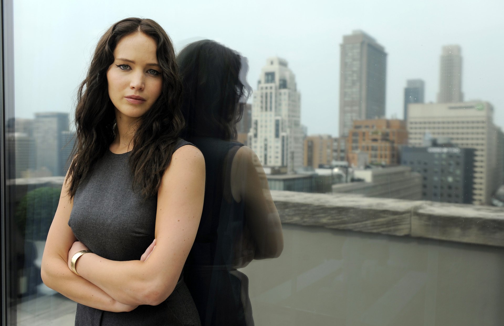 4K Ultra HD PC desktop wallpaper featuring celebrity Jennifer Lawrence standing with arms crossed by a window overlooking a cityscape.