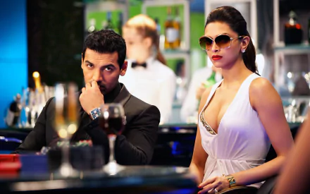 Deepika Padukone and John Abraham portrayed characters in the movie Race 2, captured in a stylish bar scene with drinks, exuding glamour and intrigue.