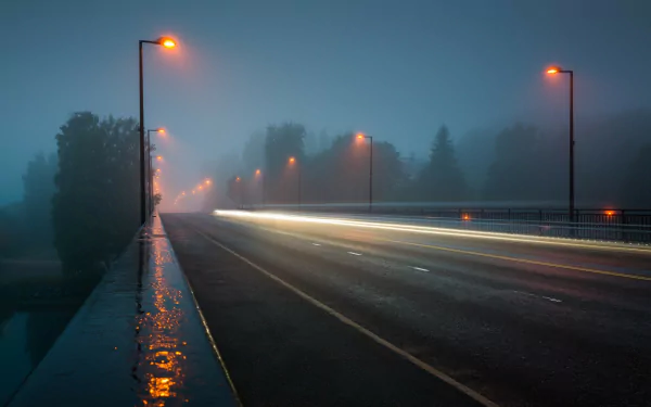 A serene night scene depicting a foggy highway illuminated by street lights, showcasing a time-lapse effect with flowing vehicle lights, creating a tranquil yet dynamic atmosphere.