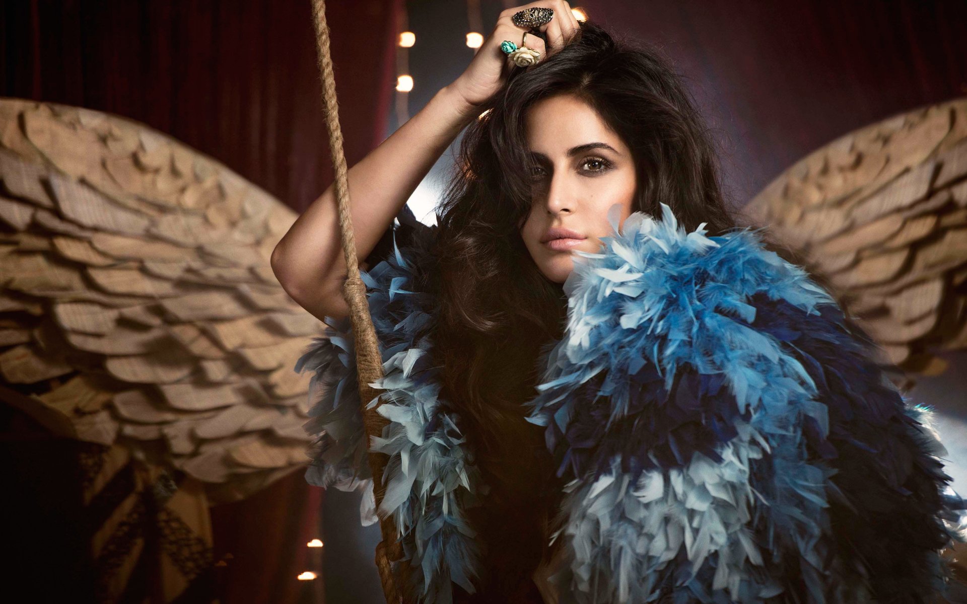 A striking HD wallpaper featuring Katrina Kaif, showcasing her with dramatic blue feathers and ethereal wings, set against a theatrical backdrop.