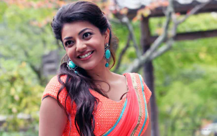 HD wallpaper featuring Kajal Aggarwal smiling in a scene from the movie Jilla, set against a lush green background.