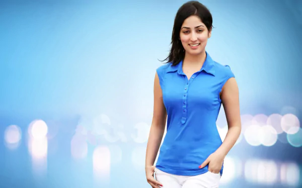 Yami Gautam, a prominent Bollywood celebrity, smiles in a vibrant blue outfit against a blurred background, creating a striking HD desktop wallpaper.